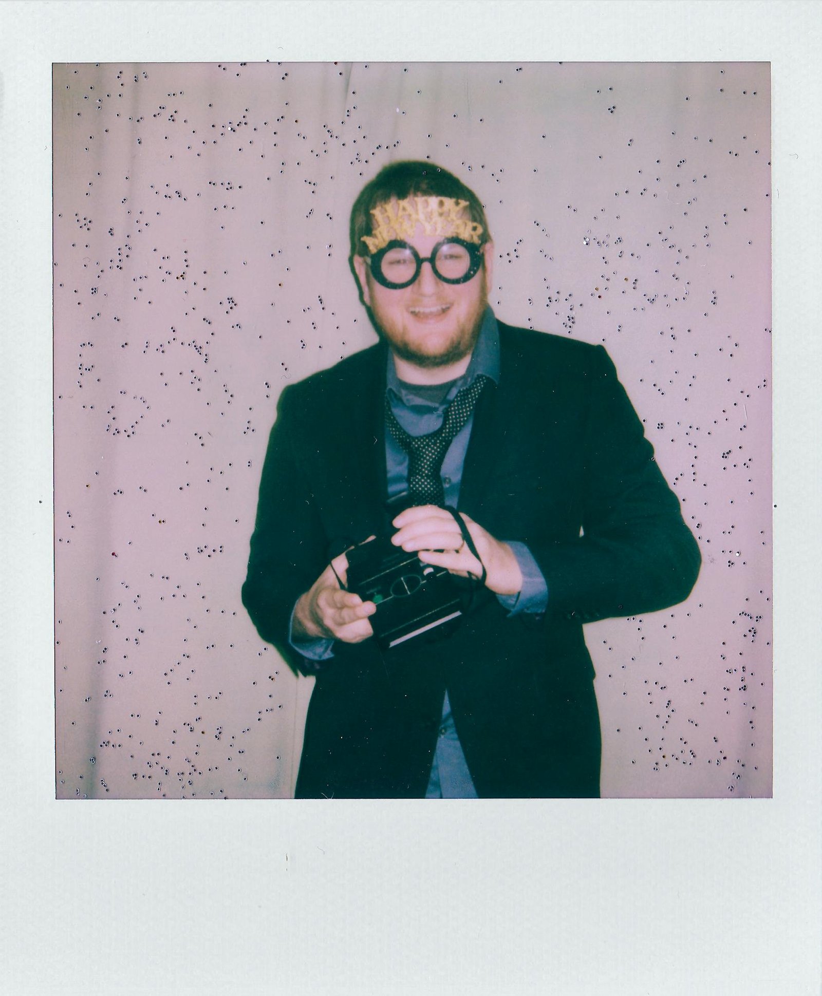 A man in a suit celebrating New Year with a Polaroid camera and confetti.
