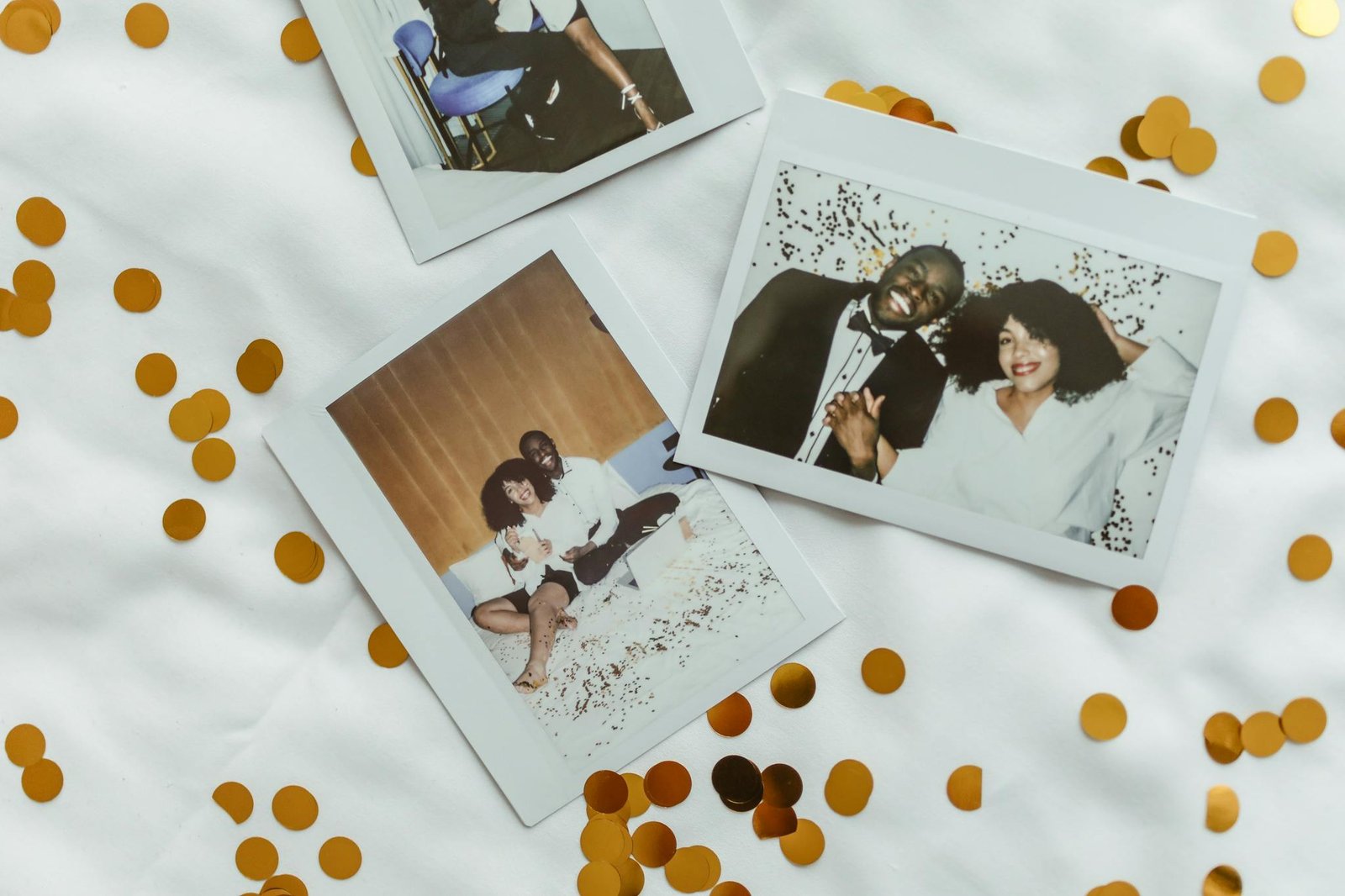 Polaroid pictures with smiling couples surrounded by gold confetti on a white fabric background.
